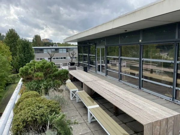 Dakterras met houten picknicktafels en groen aan de Jan Leentvaarlaan, met uitzicht op omliggende gebouwen en bomen.